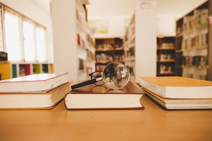 Book in library with old open textbook, stack piles of literatur